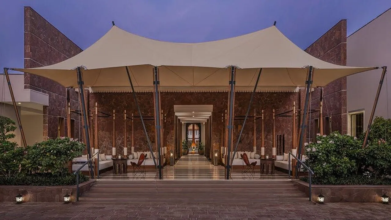 A grand entrance with a white canopy, stone walls, seating, and lit steps at dusk.