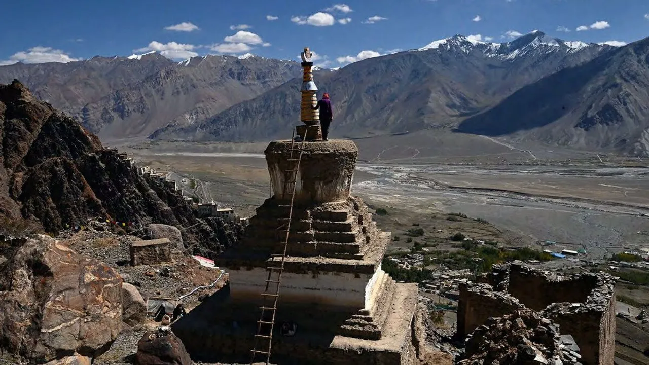 A person stands beside a Buddhist stupa overlooking a mountain valley.