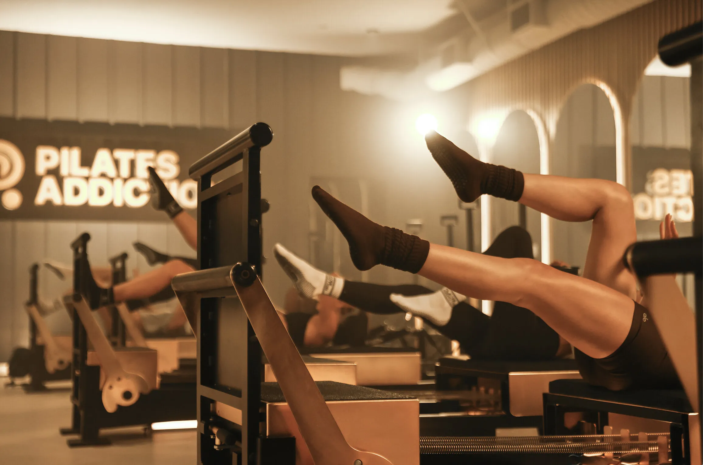 People exercising on Pilates reformer machines in a warmly lit studio.