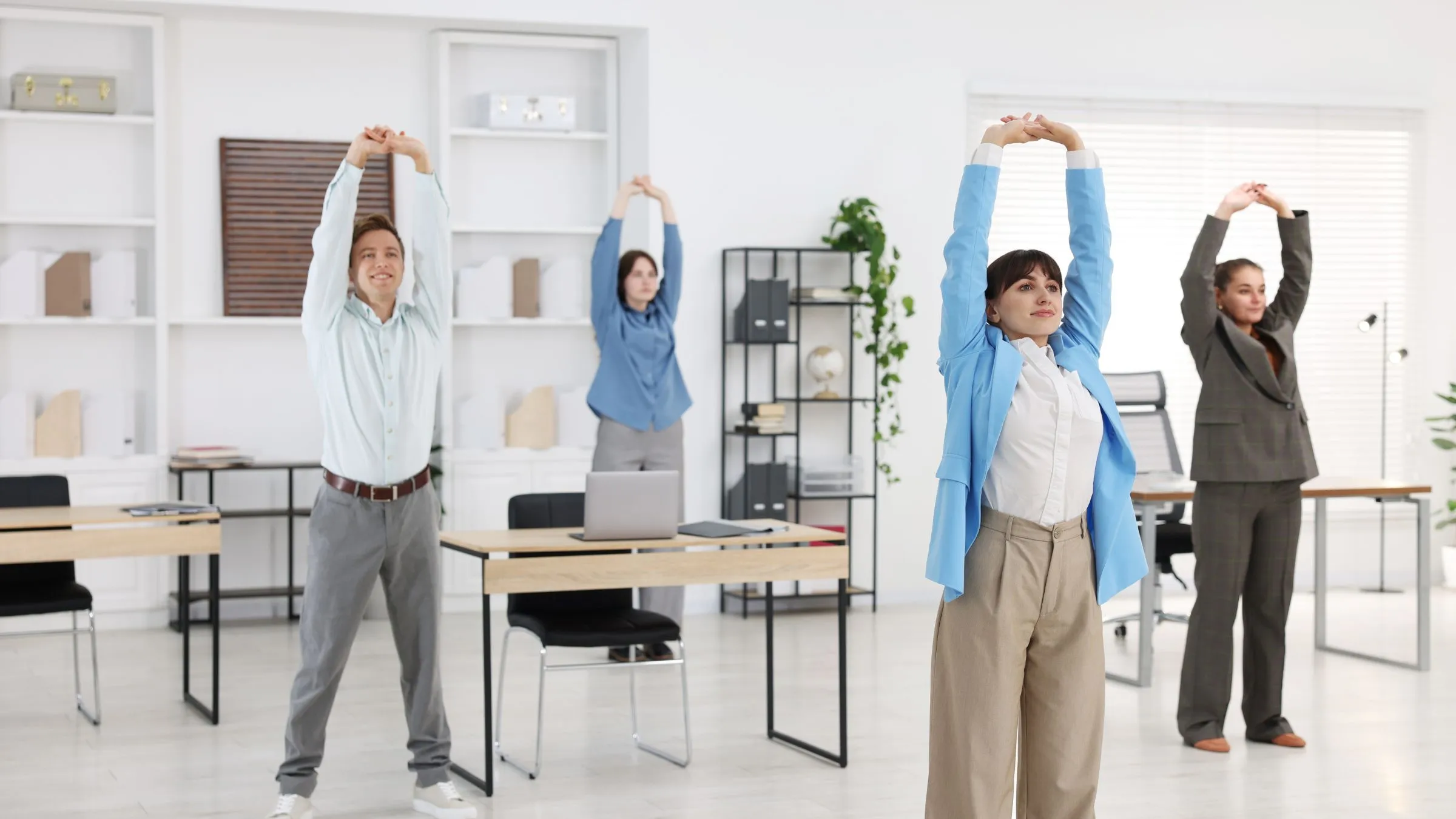 Office workers stretching their arms above their heads beside their desks.