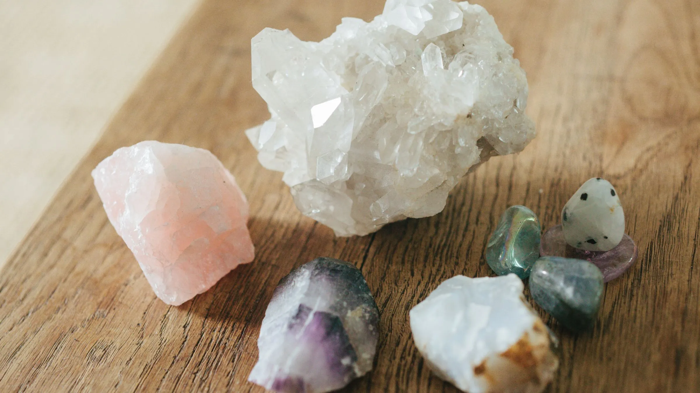 Rose quartz, clear quartz and other raw crystals on a wooden table.