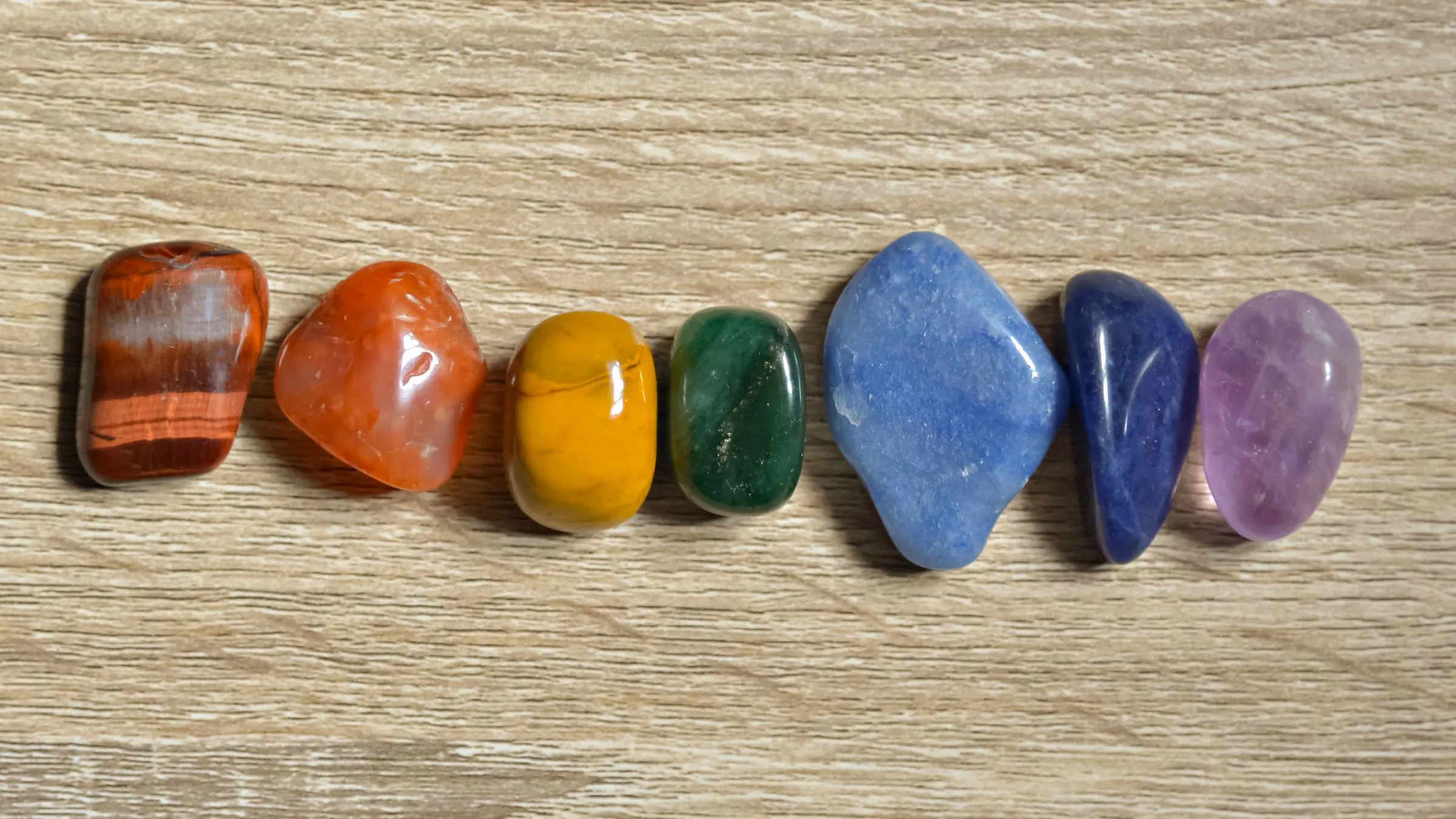 Seven polished stones in rainbow order on light wood.