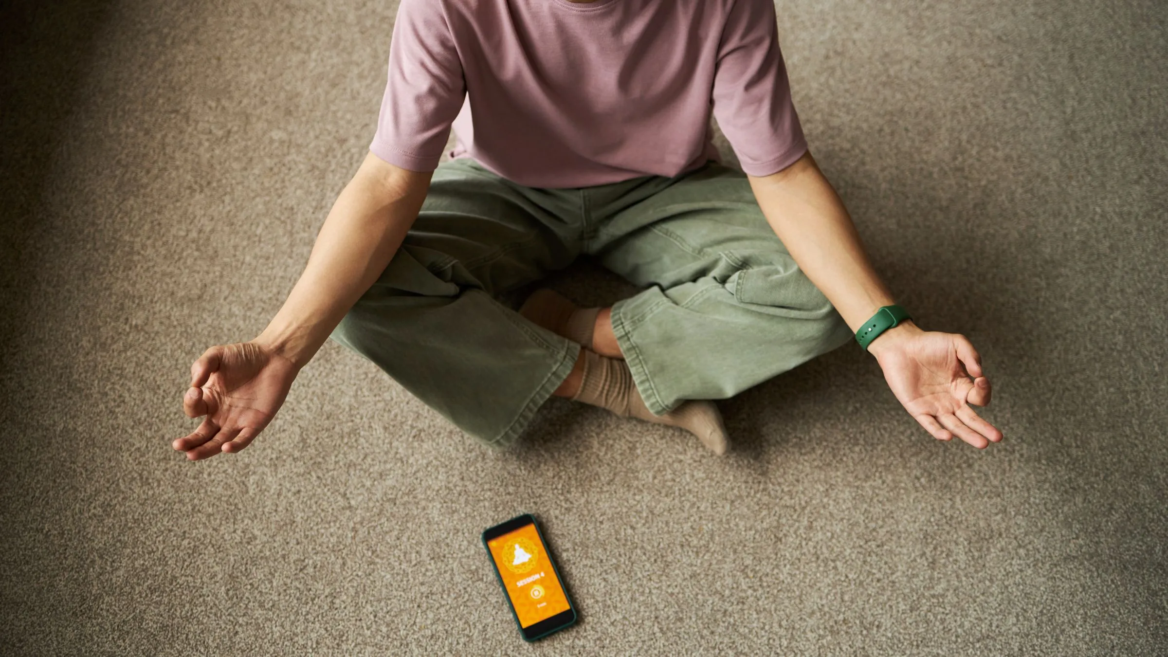 A person meditating on a carpet with a phone showing a meditation timer.