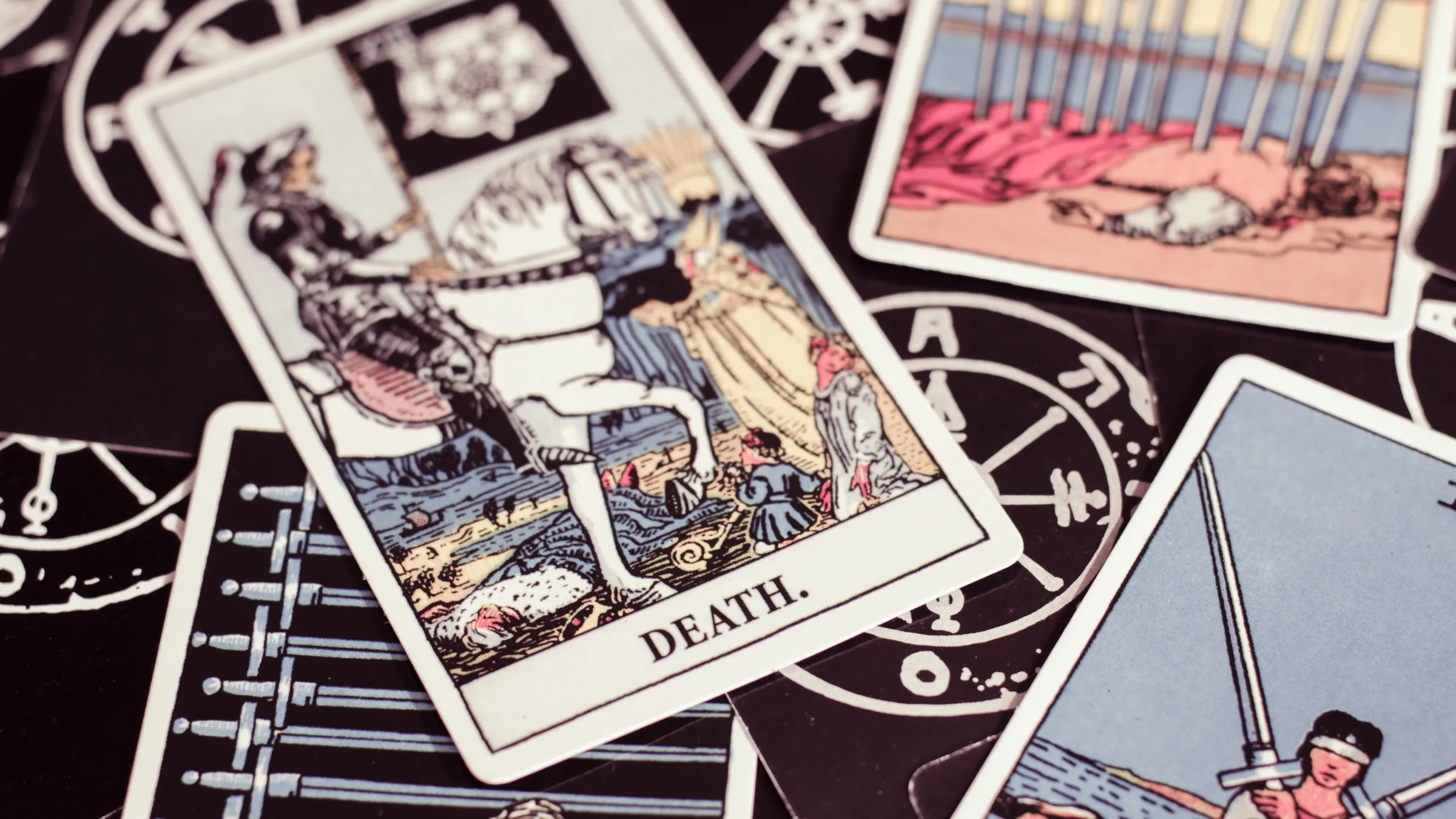 The Death tarot card among other cards on a black surface.