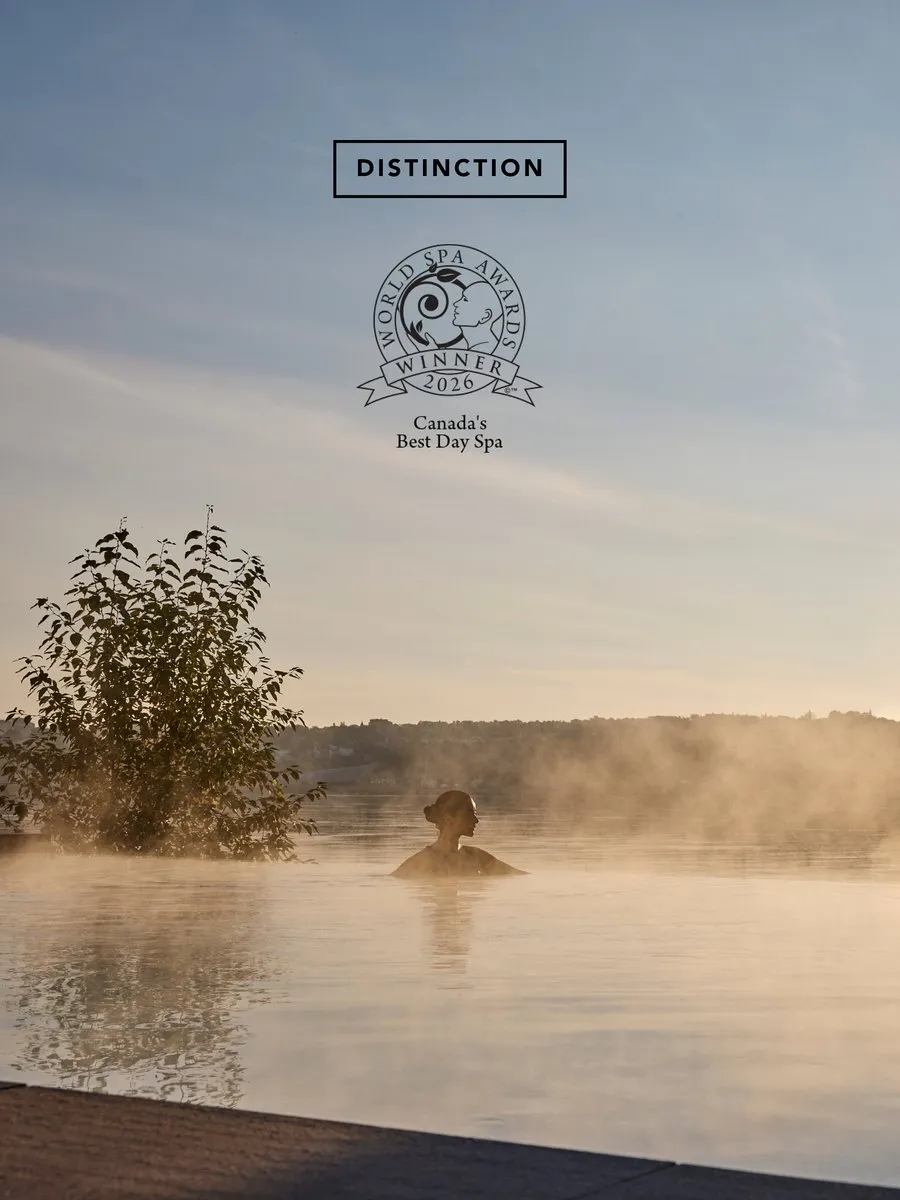 A person in a steaming outdoor pool at sunrise beneath a 2026 World Spa Awards winner logo.